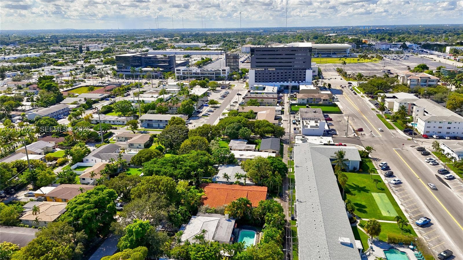 Aerial perspective of the property featuring a rectangular swimming pool, mature canopy trees, tiled roof structures, and paved road access