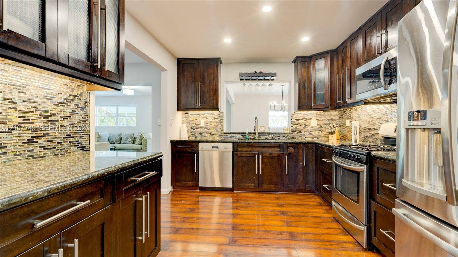 Kitchen featuring dark wood cabinetry, stainless steel appliances, multi-tonal tile backsplash, stone-surface countertops, and wood-finish flooring