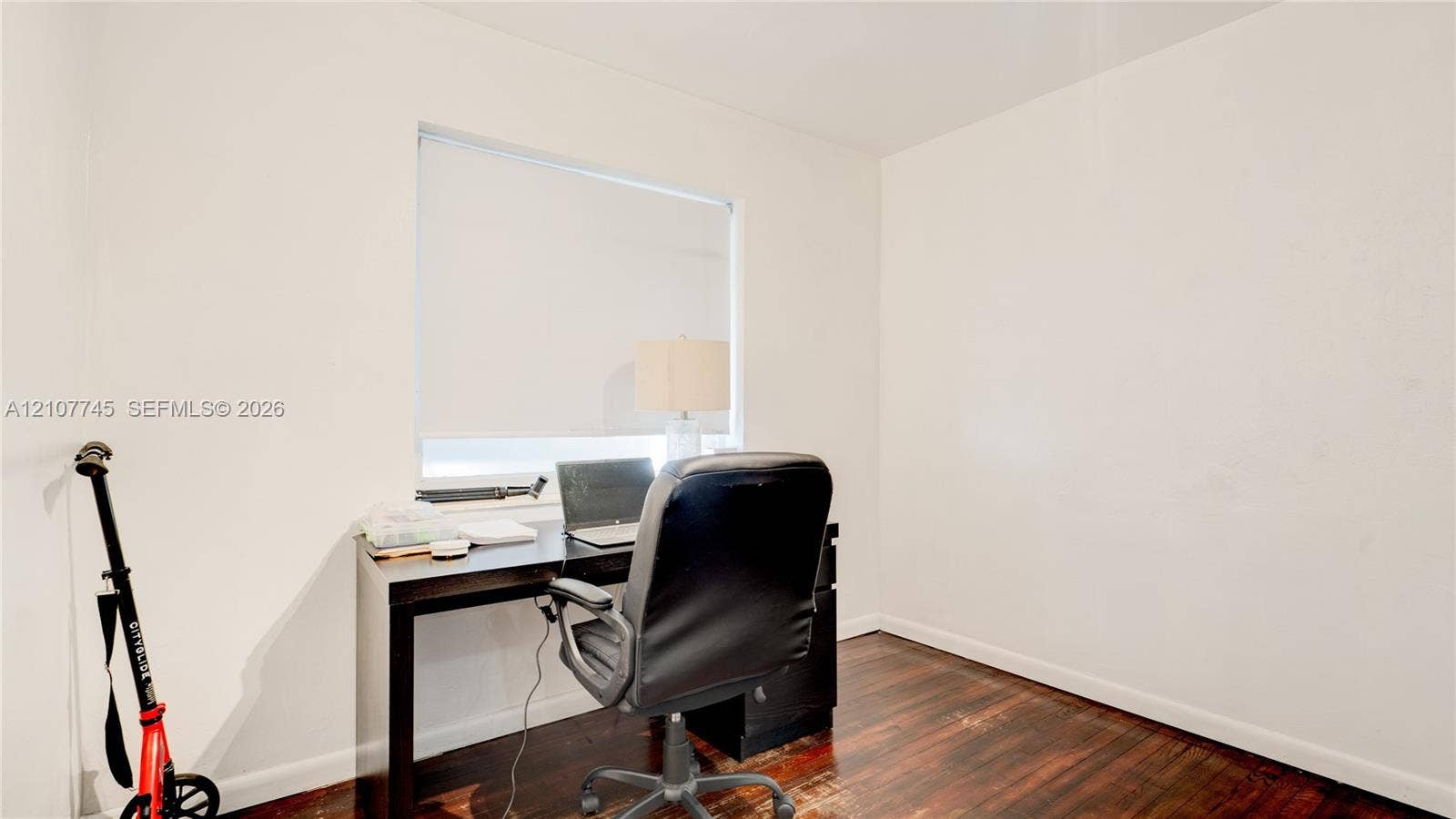 Neutral-toned interior space featuring dark wood-finish flooring and a single-pane window