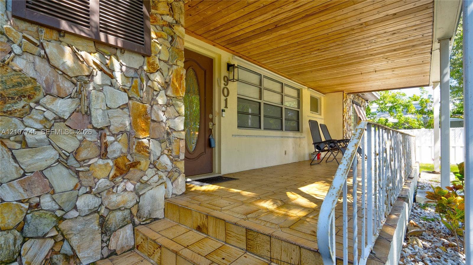 Covered porch featuring a wood-plank ceiling, natural stone facade, tiled flooring, and decorative metal railing