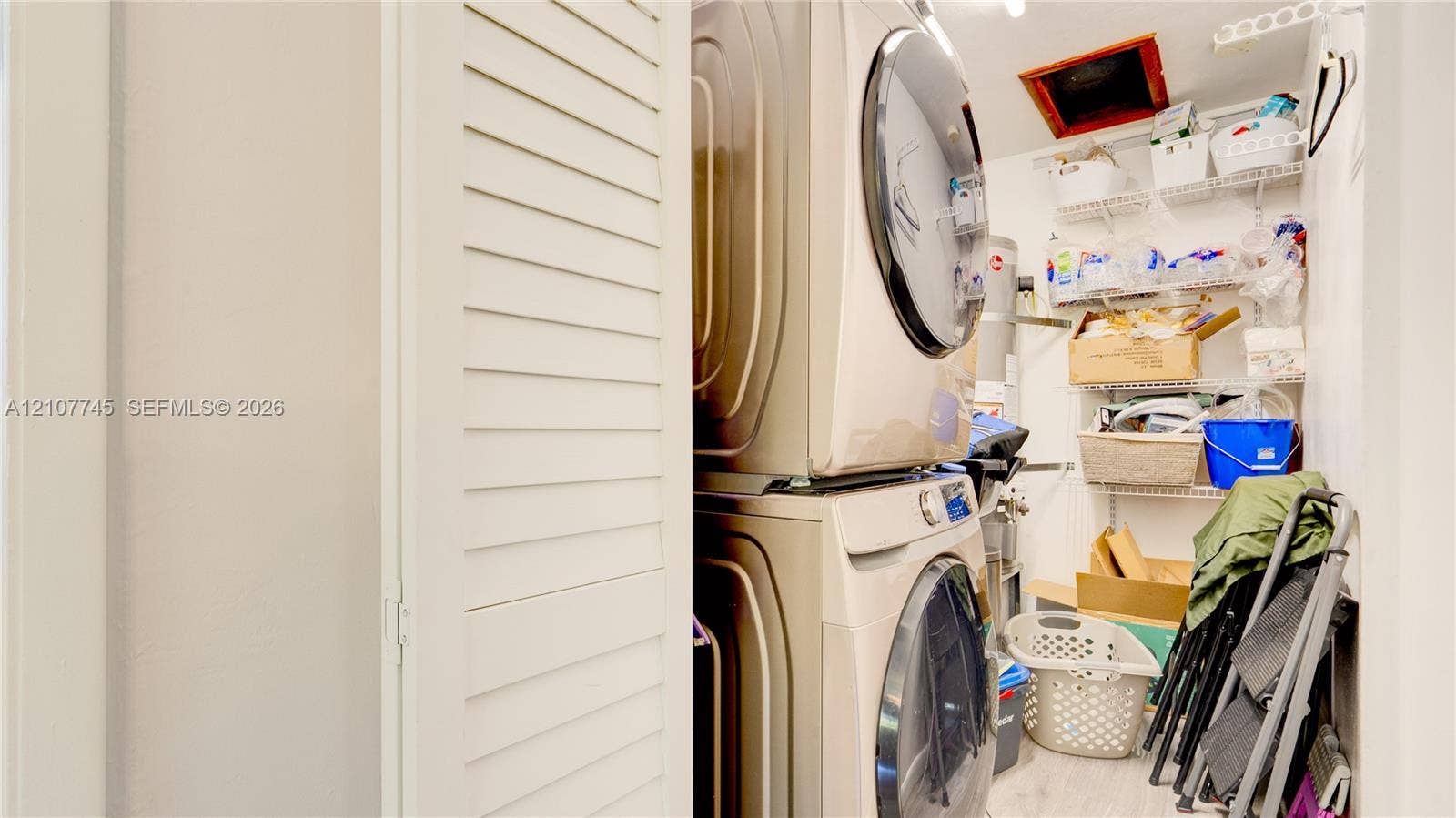 Laundry closet featuring stacked front-load appliances and tiered wire shelving