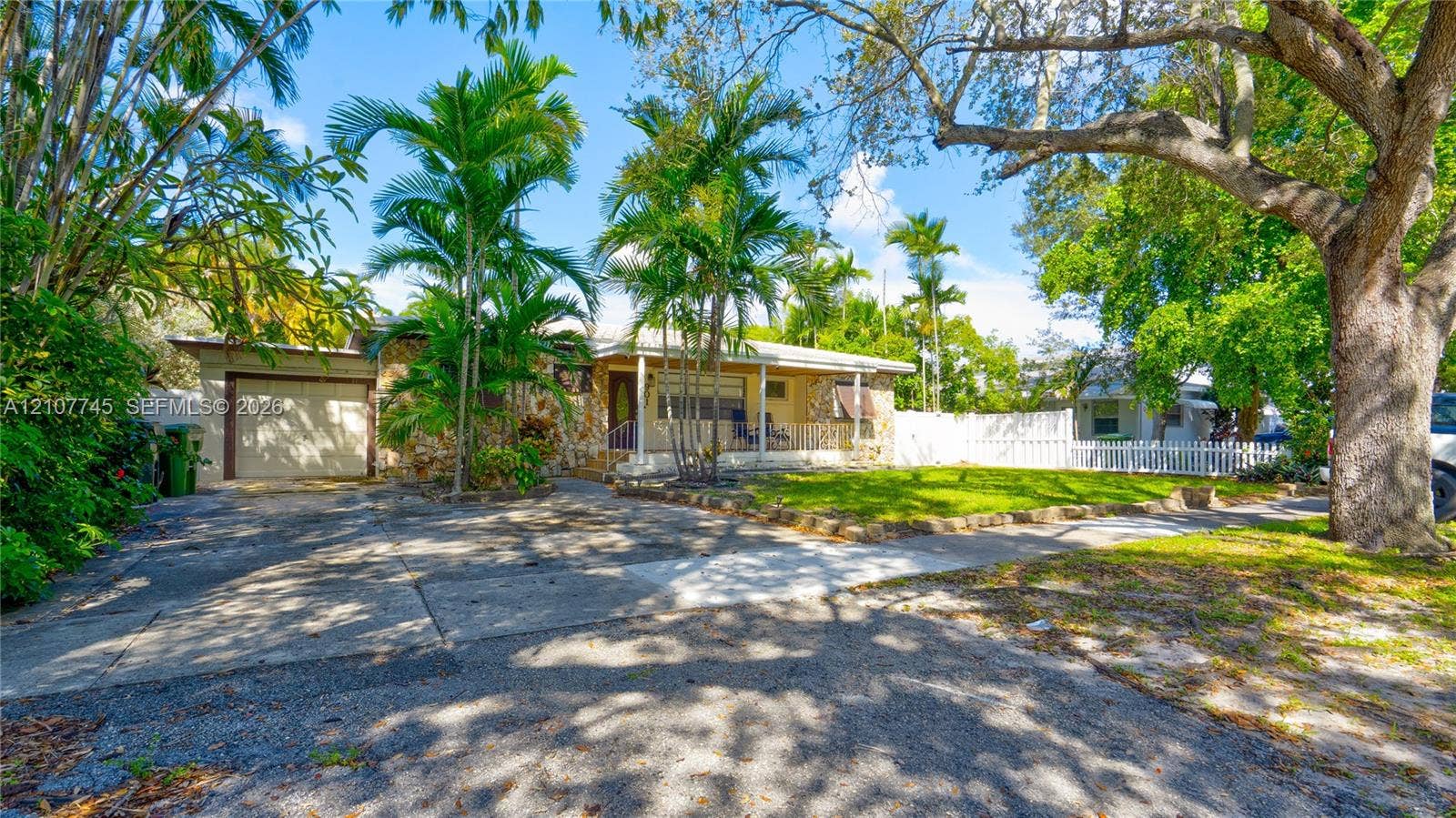 Single-story residence featuring a concrete driveway, attached one-car garage, covered front porch, and white picket fencing