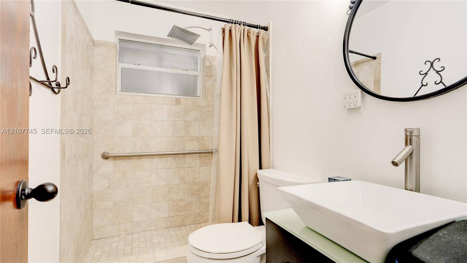 Bathroom featuring a vessel sink with a tall-profile faucet, vanity with a light-toned countertop, shower with stone-tile surround, and ceiling-mounted rainfall showerhead