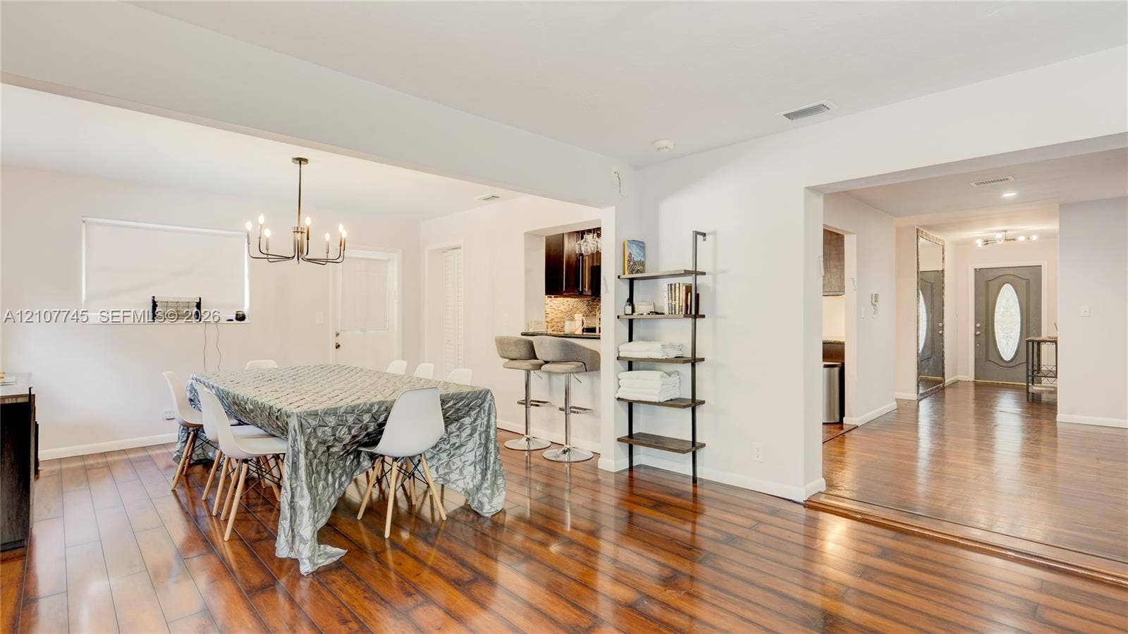 Wood-finish flooring, multi-light chandelier, pass-through breakfast bar, dark-finish cabinetry, and entry door with glass inset