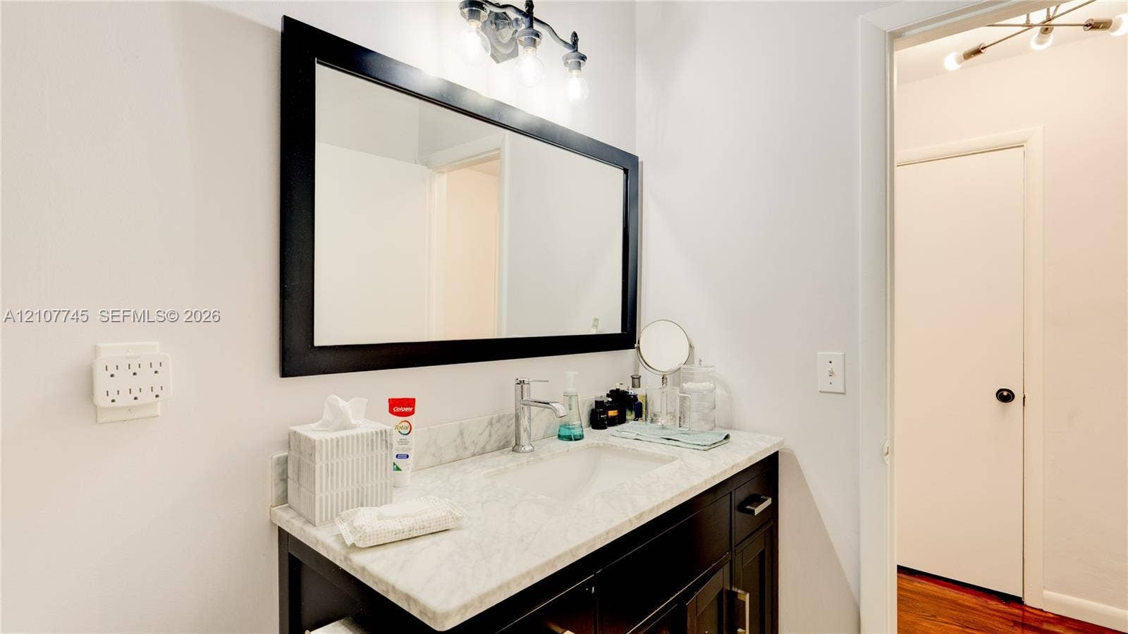 Vanity featuring a stone countertop, integrated sink, dark wood-finish cabinetry, a large framed mirror, and a multi-bulb light fixture