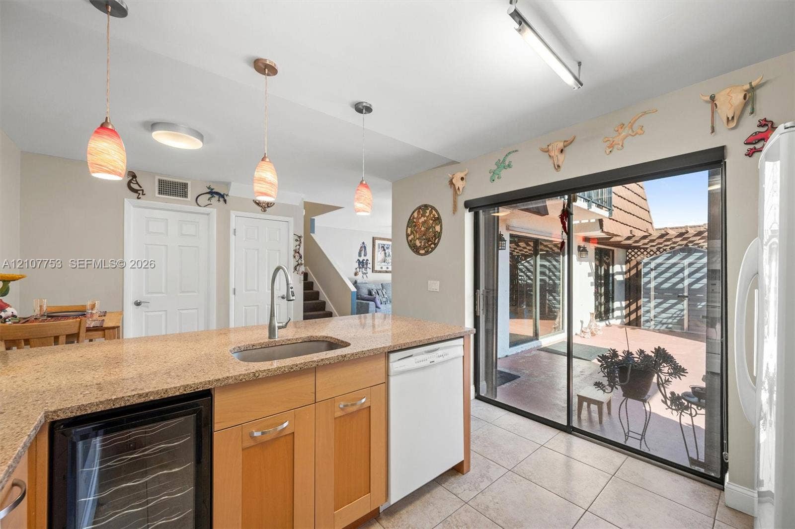 Kitchen featuring an island with a stone countertop, under-mount sink, integrated wine refrigerator, tile flooring, and sliding glass doors