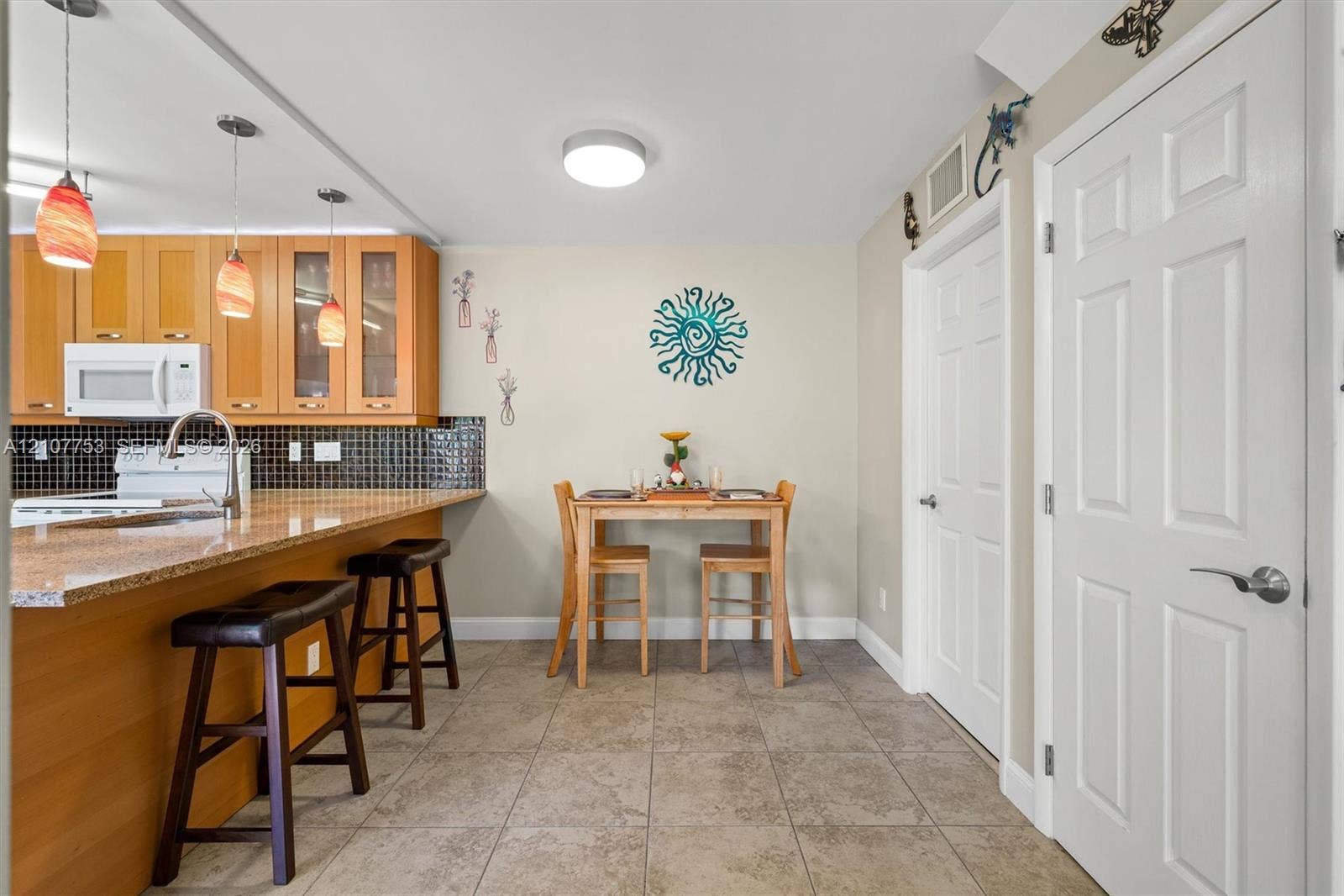 Kitchen featuring wood cabinetry, stone-finish countertops, black mosaic tile backsplash, ceramic tile flooring, and pendant lighting
