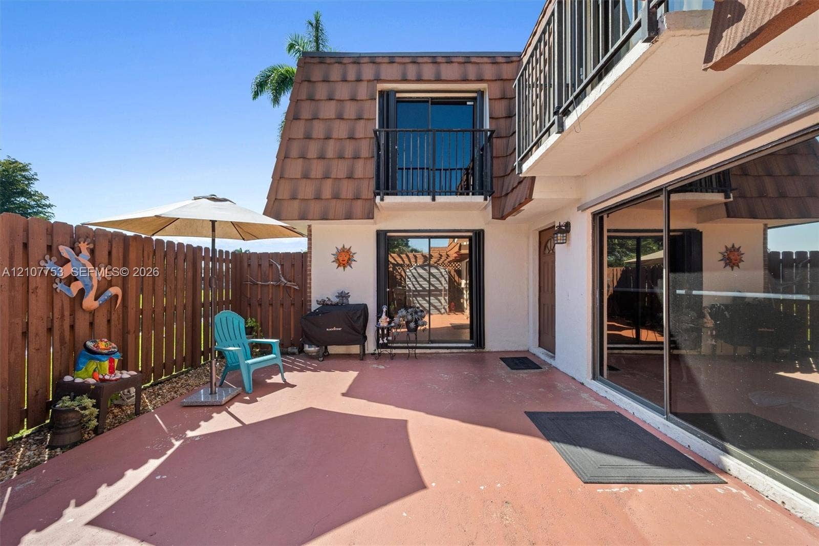 Concrete patio area enclosed by a wood privacy fence, featuring a second-story balcony with metal railing and sliding glass doors