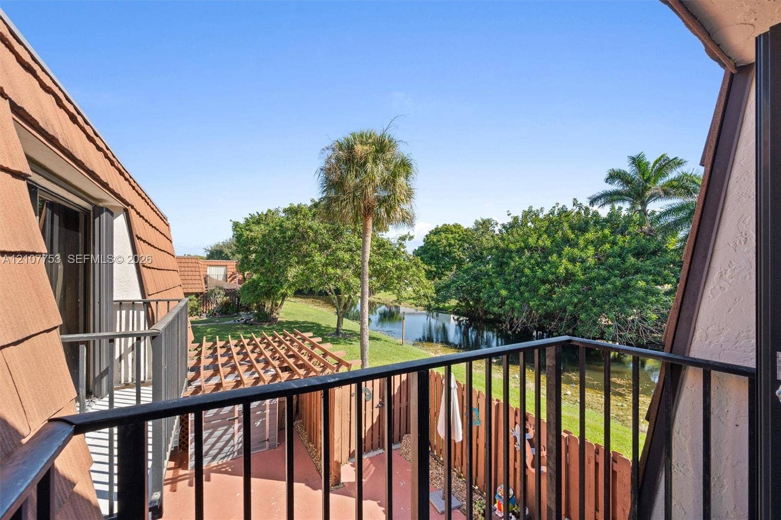 Private balcony with metal railing, clay-tile roofing, cedar-tone wooden pergola, and water frontage