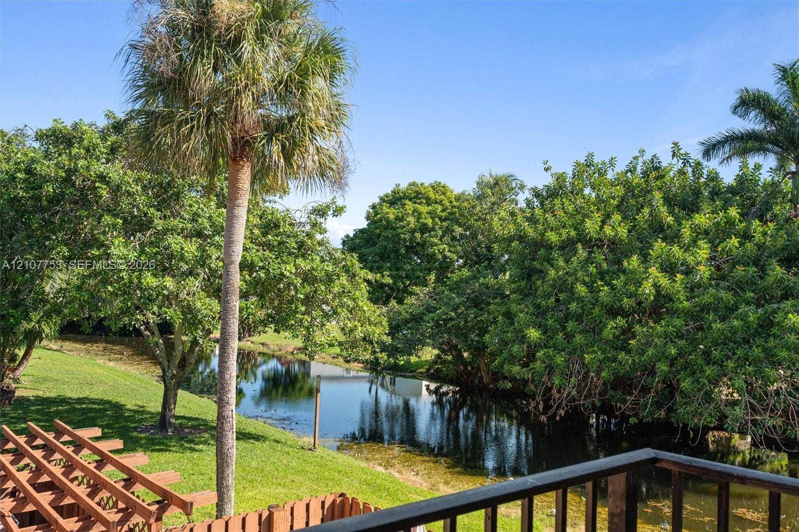 Elevated deck with wooden railings, expansive lawn, mature tropical palms, and water frontage