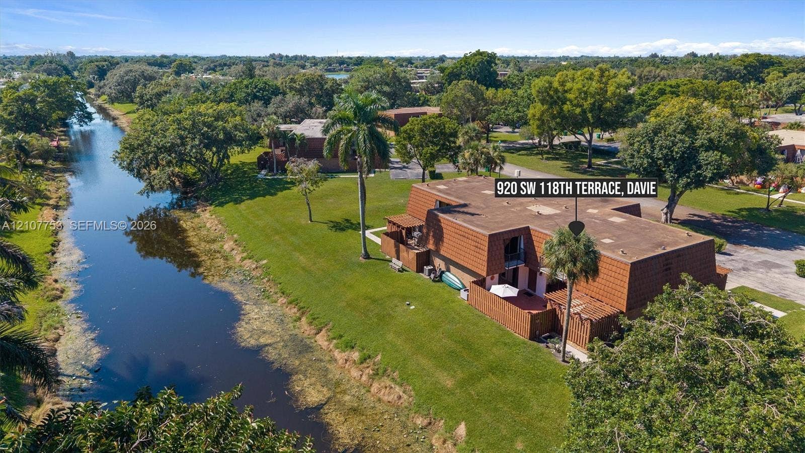 Aerial perspective of a multi-level structure featuring a mansard roof, exterior fencing, and a private patio, situated on a lot bordering a canal