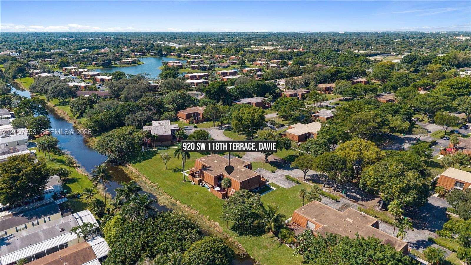 Aerial perspective of multi-story masonry residential building featuring expansive landscaped grounds, mature trees, and direct canal frontage