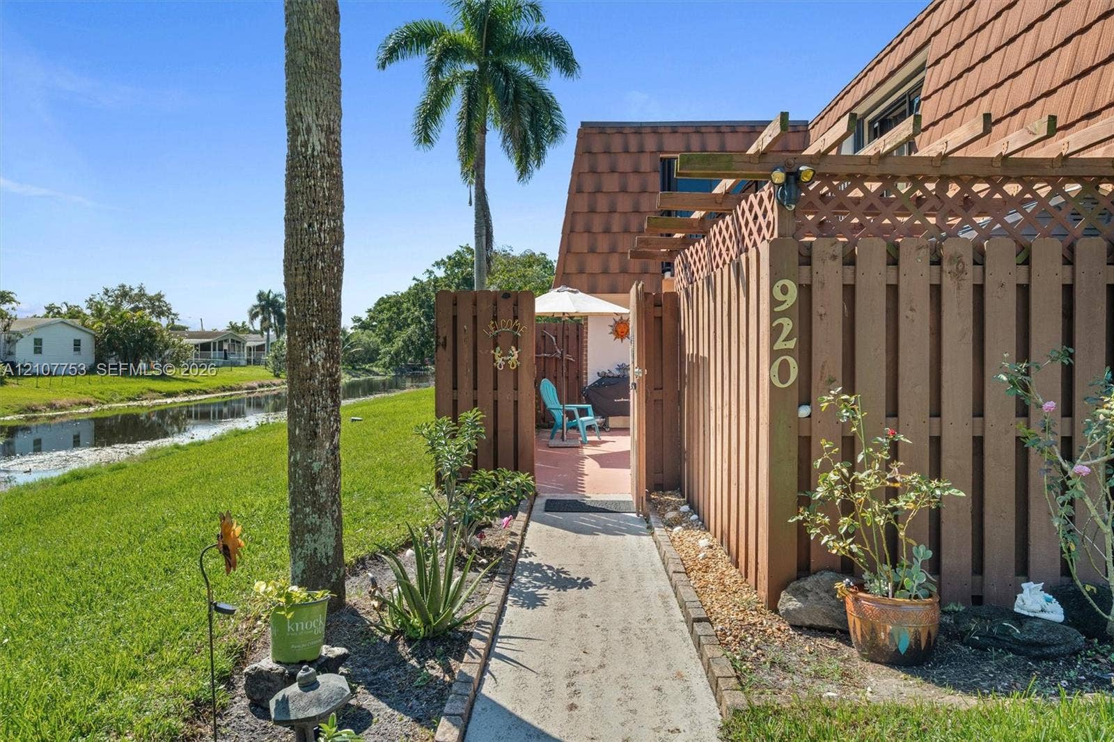 Exterior entry featuring a private wood fence, pergola, concrete walkway, and shingled roofline, situated along a waterway