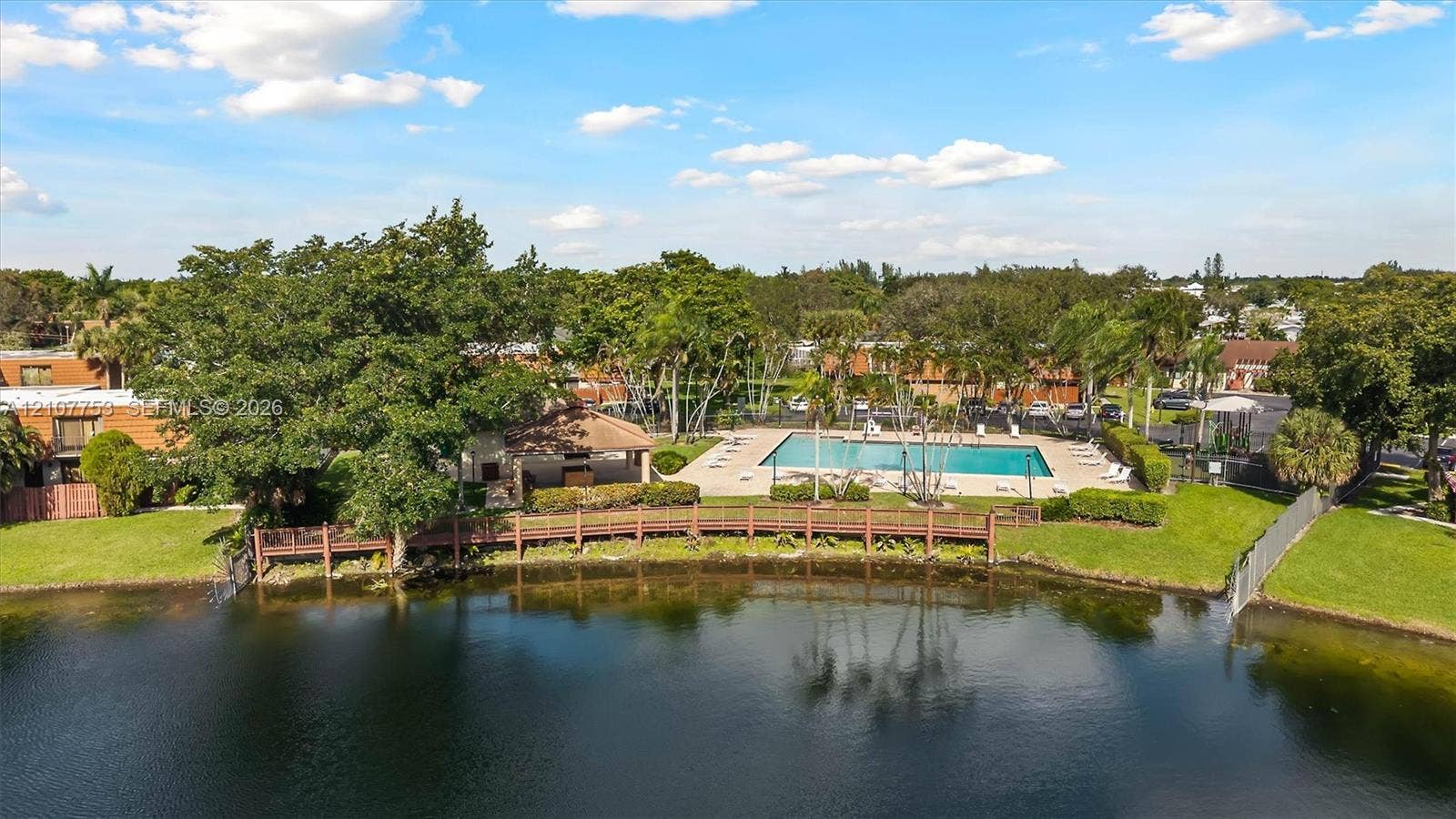 Waterfront area featuring a swimming pool, covered pavilion, wooden boardwalk, and mature landscaping
