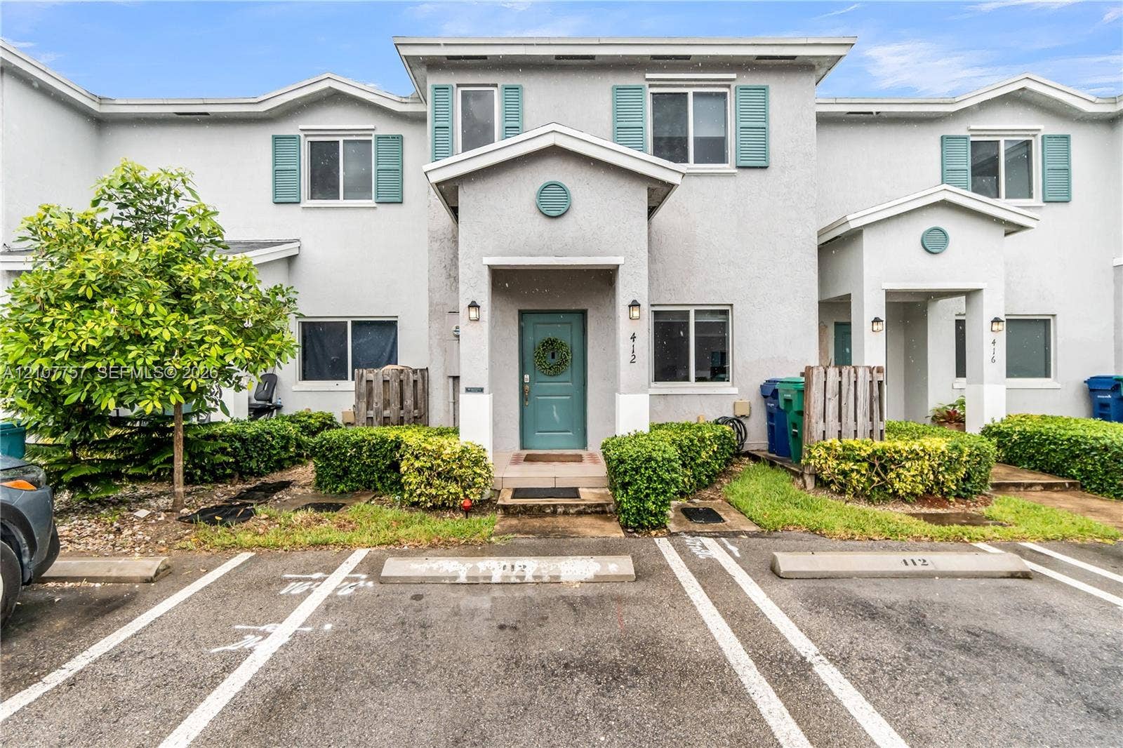 412 NW 12th Avenue, Florida City, FL 33034 Two-story stucco exterior featuring gabled rooflines, teal window shutters, and assigned parking spaces