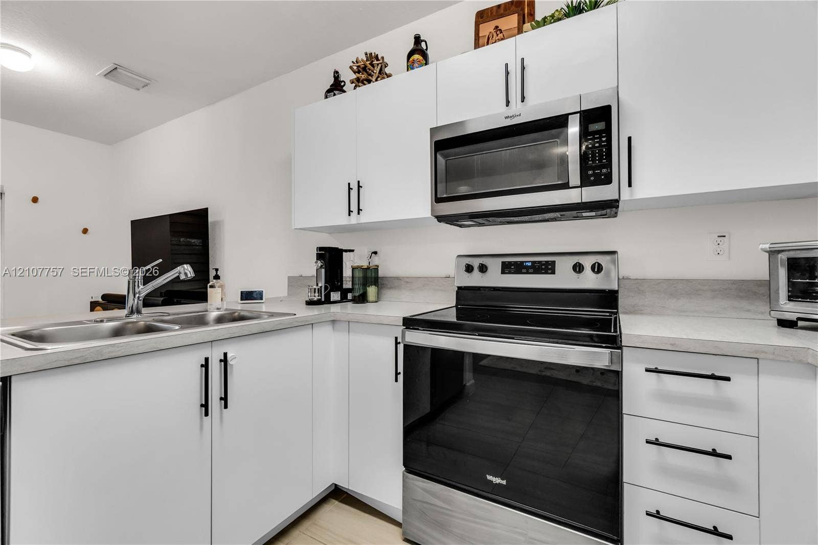 412 NW 12th Avenue, Florida City, FL 33034 Kitchen featuring white shaker-style cabinetry, matte black hardware, stainless steel appliances, and solid-surface countertops with an integrated dual-basin sink