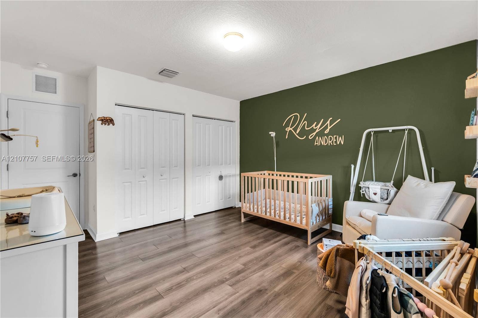 412 NW 12th Avenue, Florida City, FL 33034 Room featuring wood-finish flooring, two sets of double-door closets, and an accent wall finished in a deep olive tone
