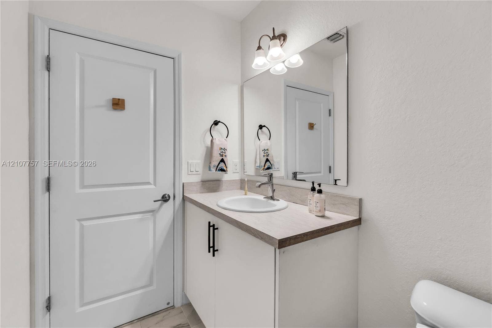 412 NW 12th Avenue, Florida City, FL 33034 Vanity featuring a neutral-tone countertop, an integrated sink, matte black hardware, a large wall-mounted mirror, and multi-bulb decorative lighting