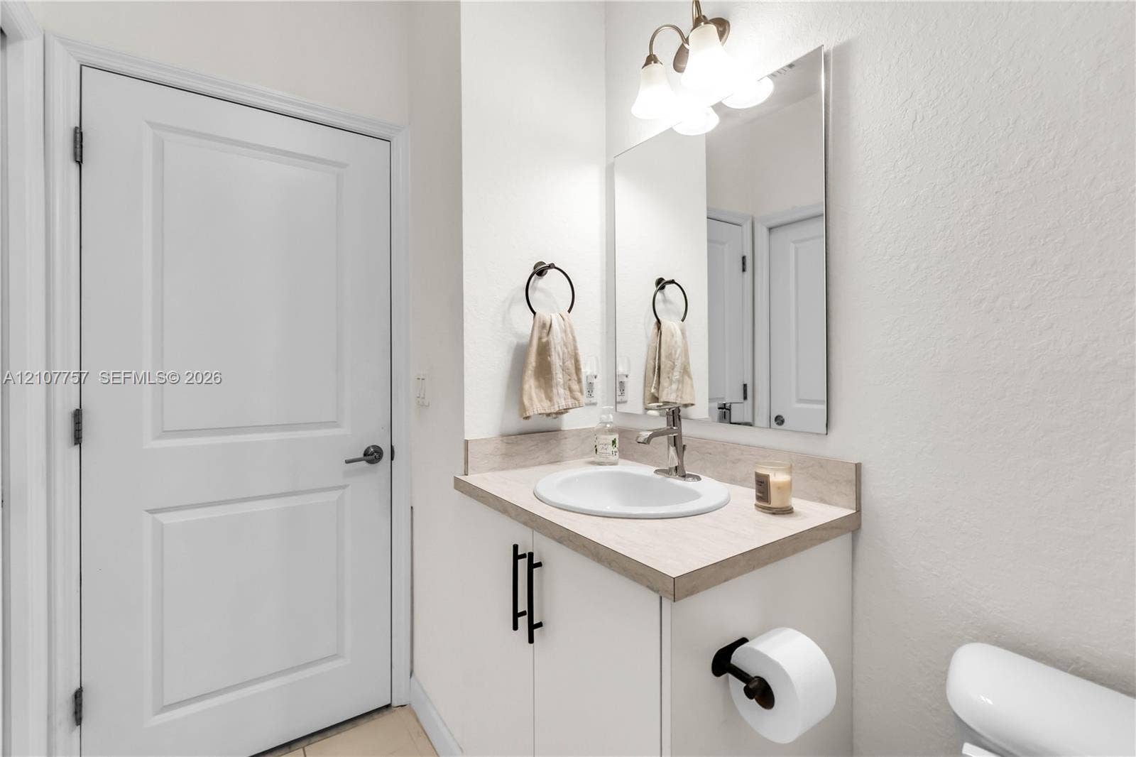 412 NW 12th Avenue, Florida City, FL 33034 Vanity featuring a light-toned countertop, undermount oval sink, matte black hardware, and an attached three-light fixture above a rectangular mirror