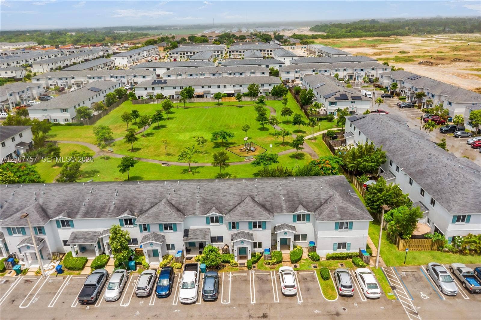 412 NW 12th Avenue, Florida City, FL 33034 Aerial perspective of a multi-unit residential complex featuring light-toned siding, dark shingle roofs, designated surface parking, and extensive landscaped green space with paved pedestrian walkways