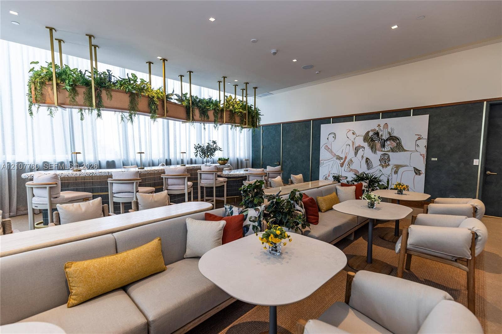 Common area featuring floor-to-ceiling windows with sheer drapery, a stone-topped bar with brass-tone pendant hardware, integrated overhead planters, textured dark accent walls, and recessed lighting