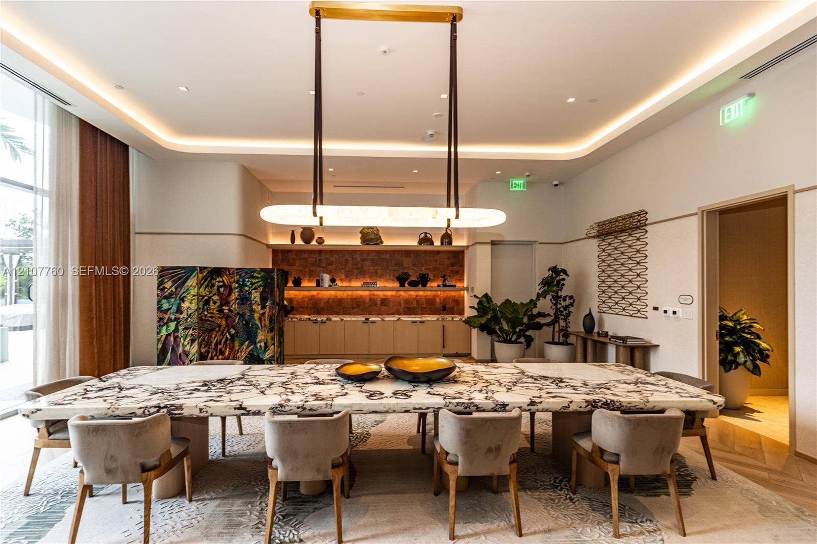 Custom stone-topped table, linear suspended light fixture, recessed tray ceiling with integrated cove lighting, and built-in cabinetry with stone-finish backsplash