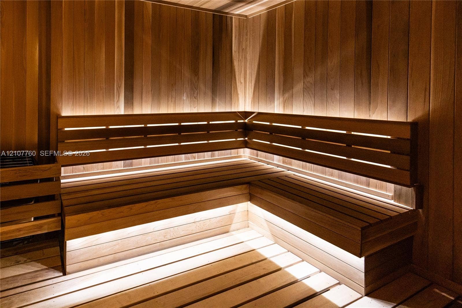 Custom cedar-paneled sauna featuring tiered L-shaped benches, integrated linear accent lighting, and a wall-mounted heater unit