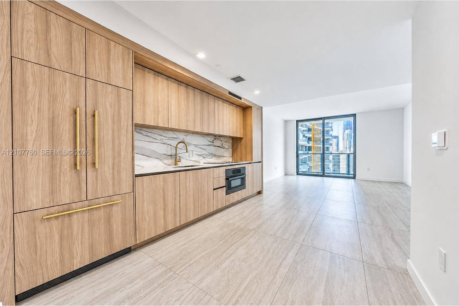 Kitchen featuring custom wood-finish cabinetry, stone-patterned backsplash, integrated appliances, brass-tone hardware, and large-format tile flooring