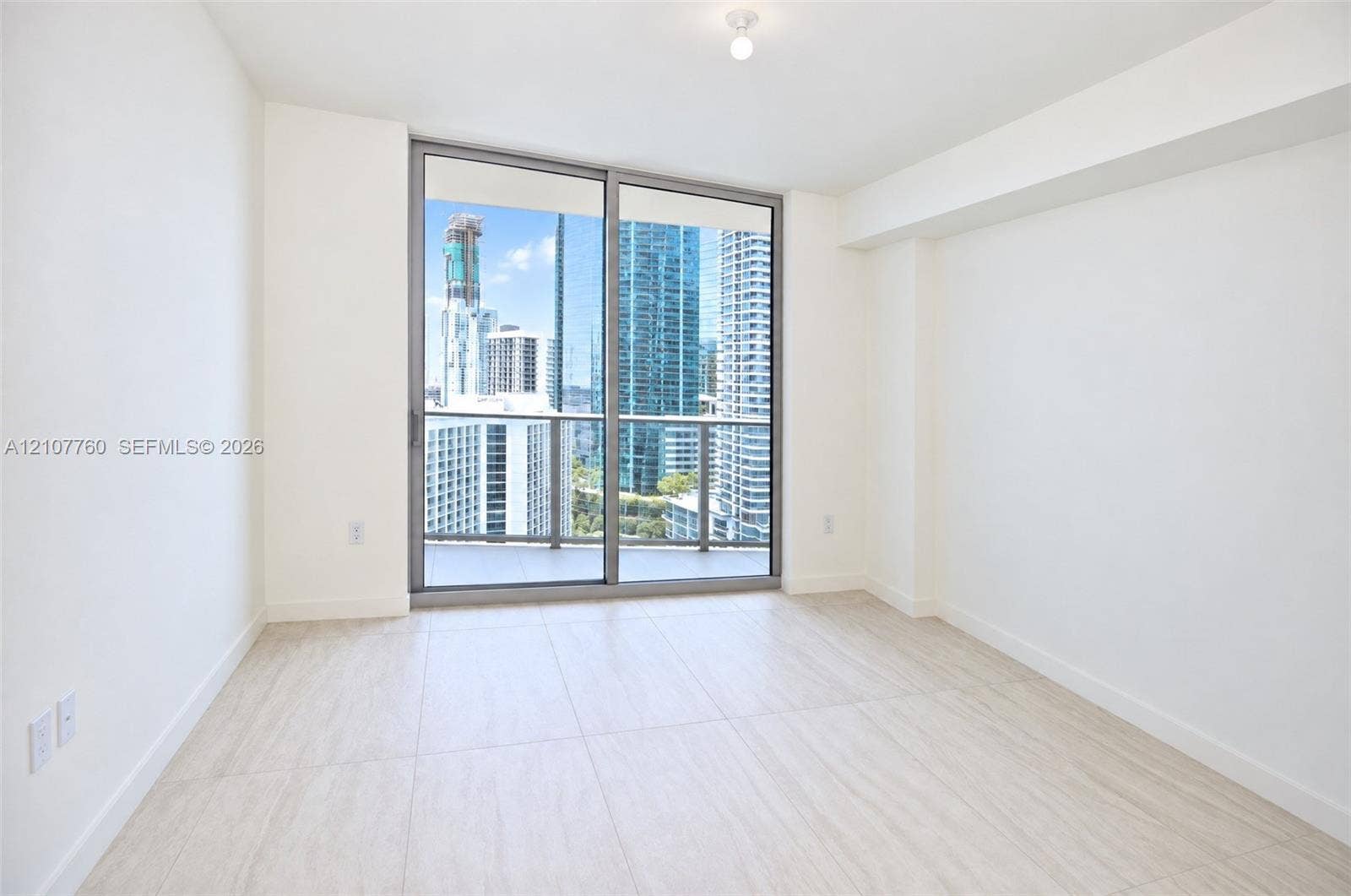 Floor-to-ceiling sliding glass doors, neutral tile flooring, and urban skyscraper scenery