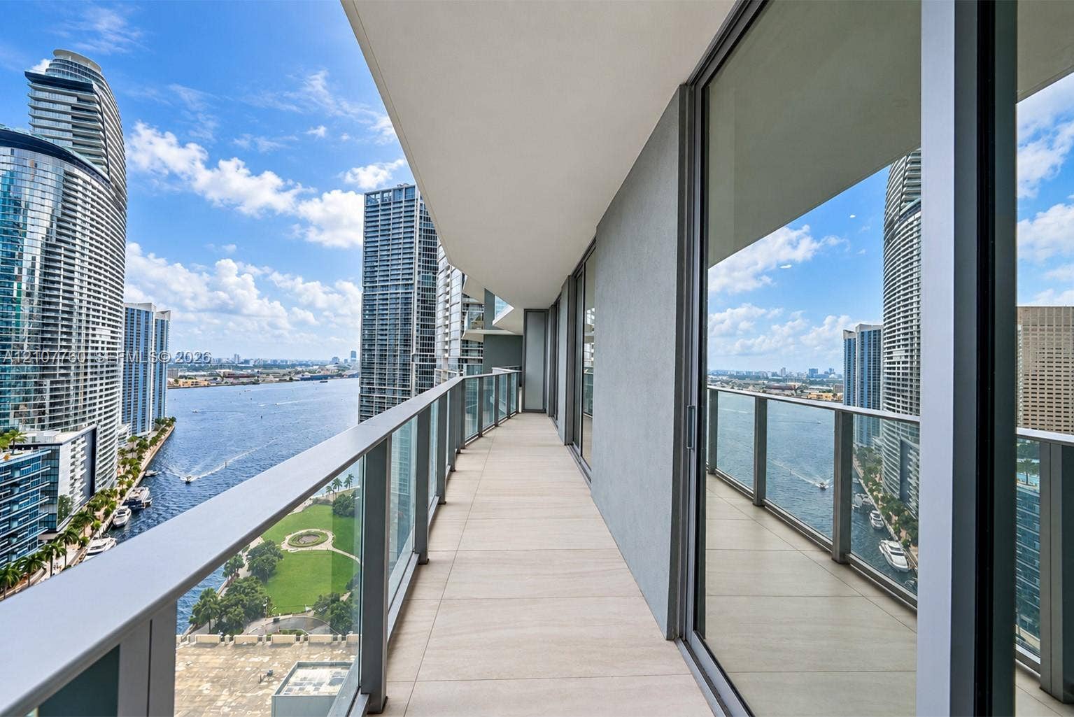 Expansive covered balcony featuring large-format tile flooring, glass panel railings, and floor-to-ceiling sliding glass entry points