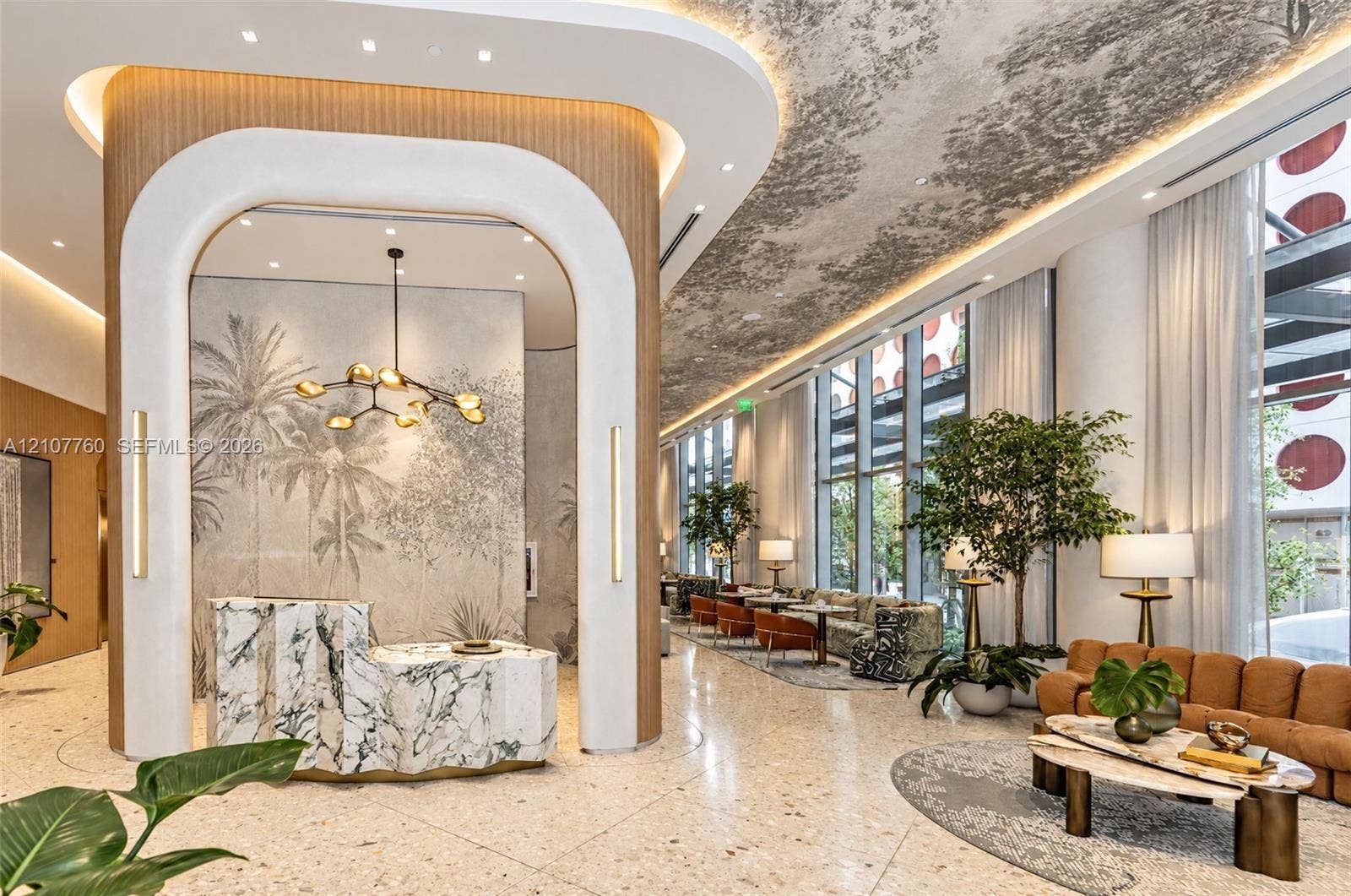 Grand lobby featuring floor-to-ceiling windows, arched architectural detailing with wood-finish paneling, a textured stone reception desk, integrated recessed lighting, and patterned ceiling finishes