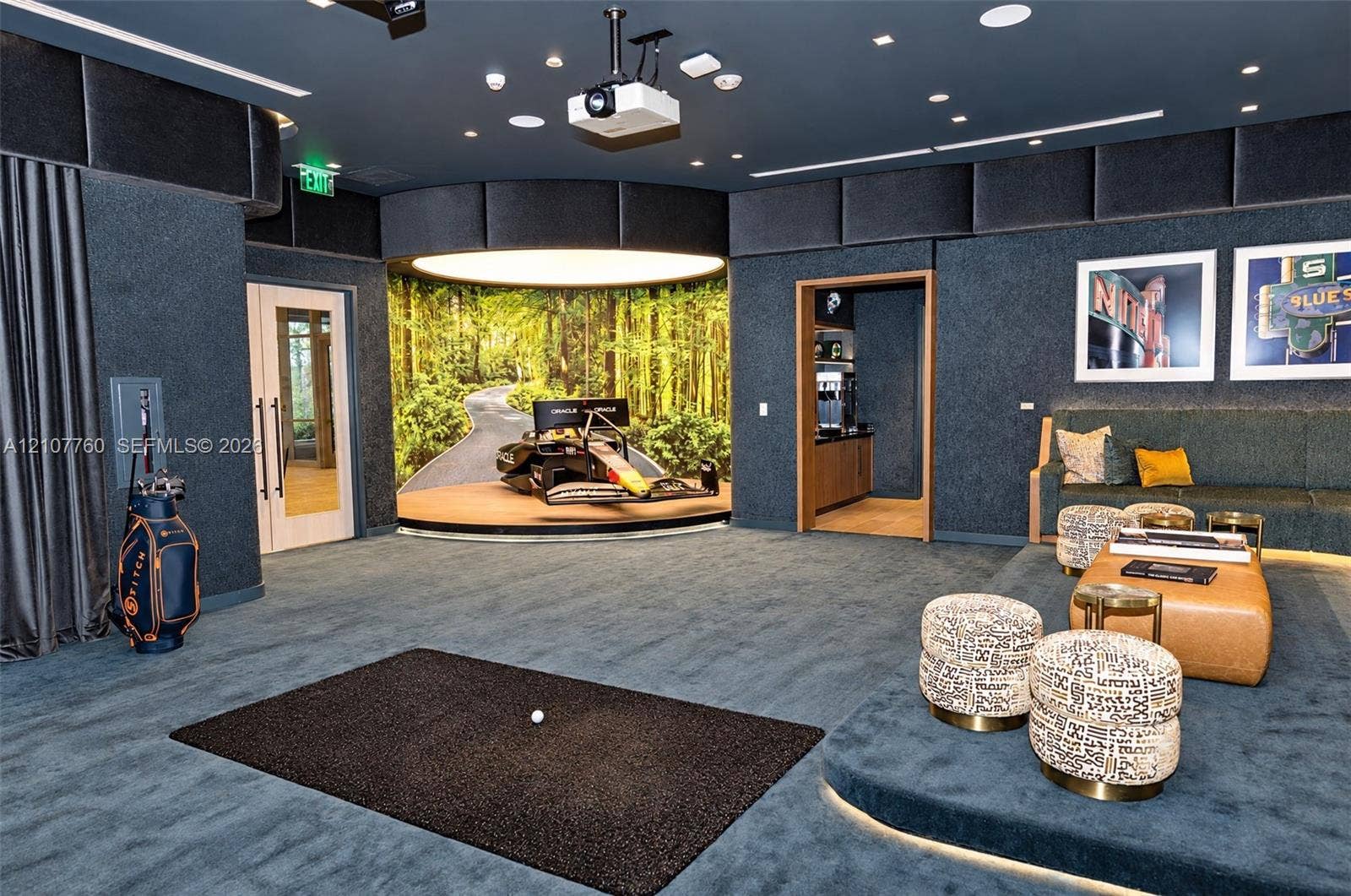 Custom media room featuring acoustical wall paneling, a recessed circular stage with integrated lighting, overhead projection system, elevated platform seating area, and inset wet bar