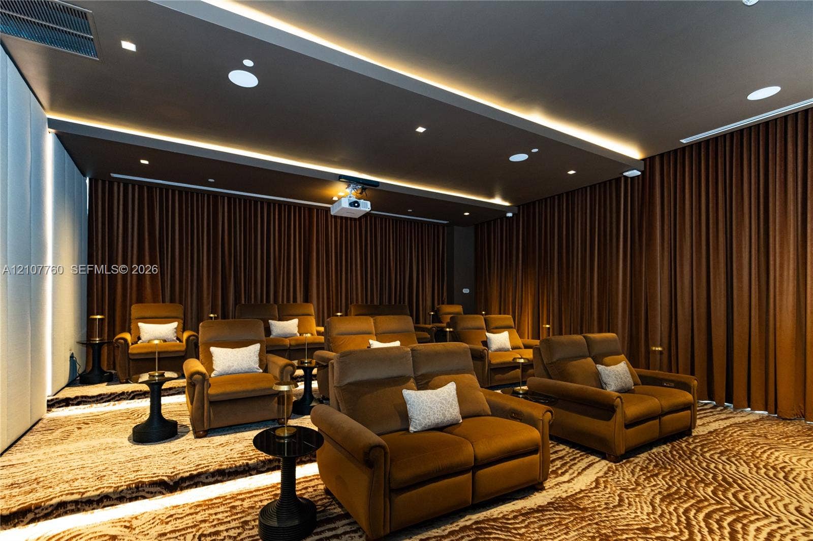 Media room featuring a tray ceiling with recessed lighting, tiered flooring, wall-to-wall drapery, and a ceiling-mounted projector