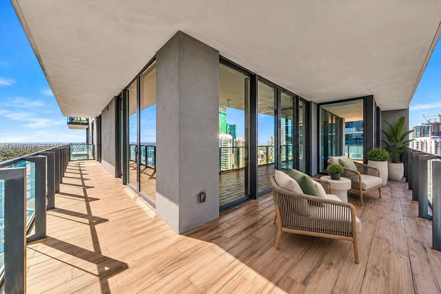 Covered wraparound balcony featuring wood-finish tile flooring, glass panel railings, and floor-to-ceiling glass doors