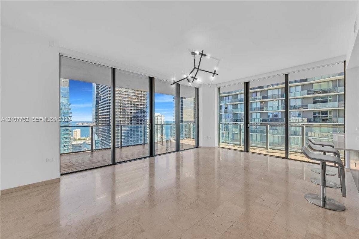 Floor-to-ceiling windows, wrap-around balcony, polished stone flooring, and architectural geometric chandelier