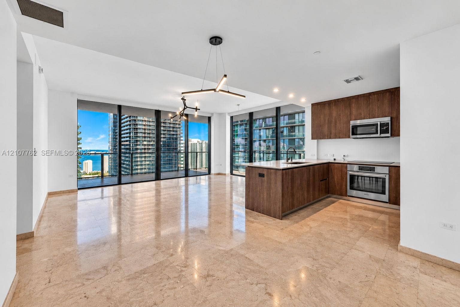Open-concept interior featuring natural stone flooring, floor-to-ceiling windows, modern cabinetry, a kitchen island with stone countertops, and contemporary geometric lighting