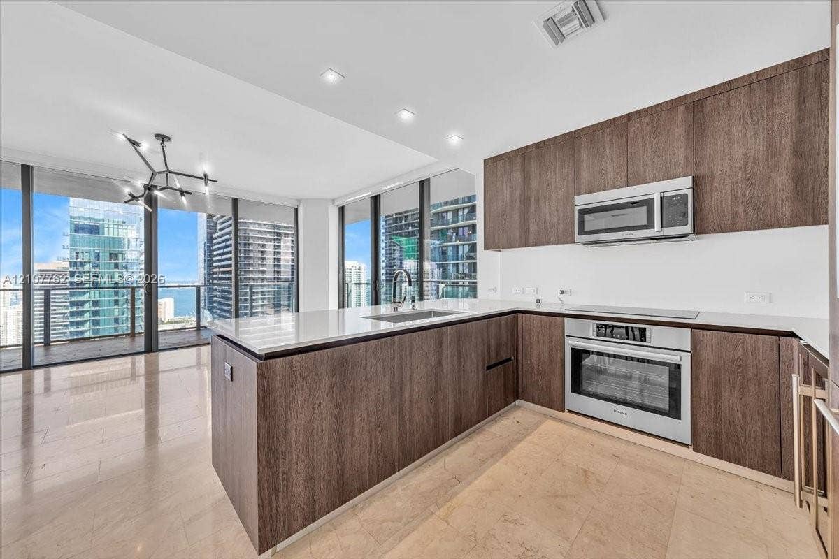 Kitchen featuring wood-finish cabinetry, stone countertops, stainless steel appliances, tile flooring, and floor-to-ceiling windows