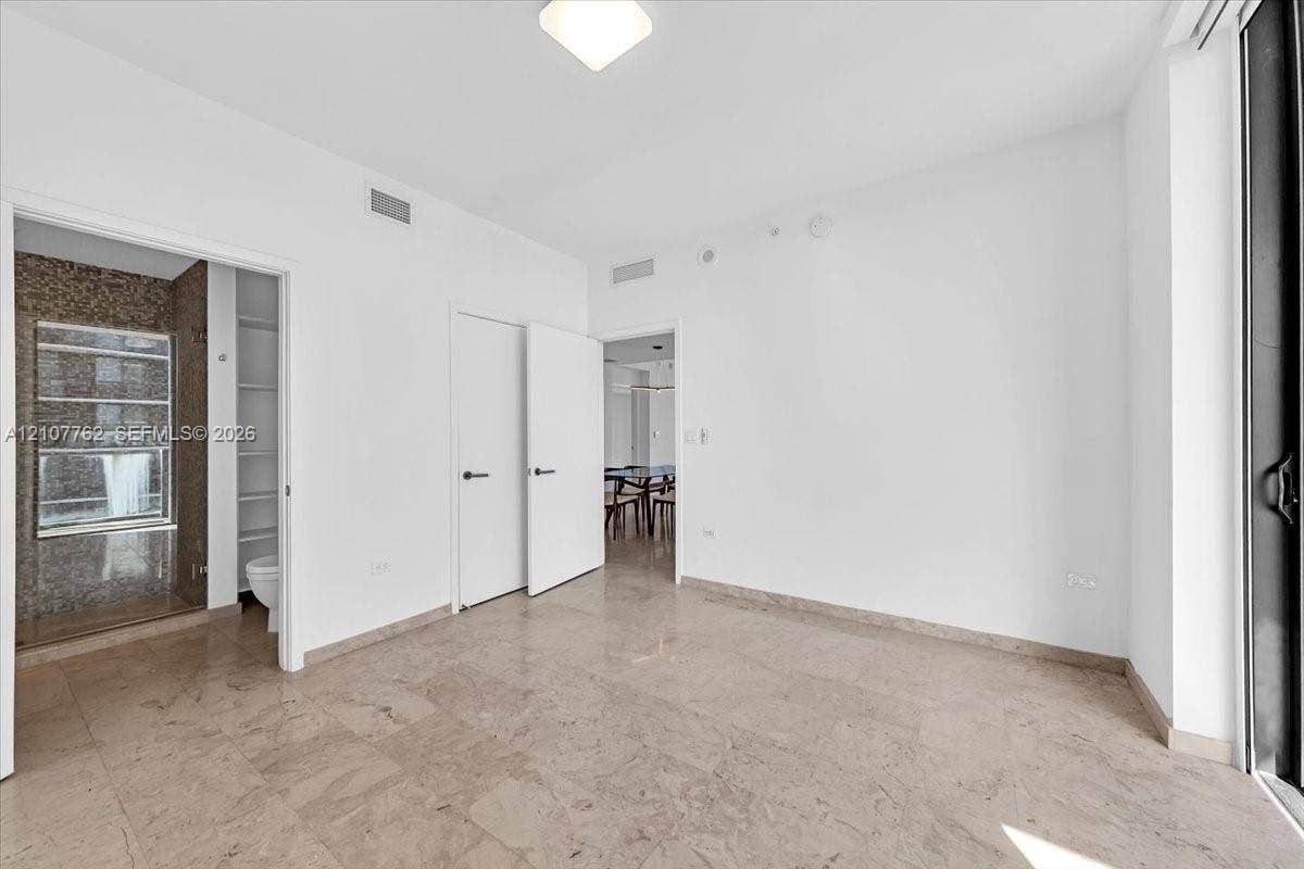 Interior room featuring large-format stone tile flooring, neutral wall finishes, solid-core interior doors with matte black hardware, and an attached bathroom with tiled wall accents