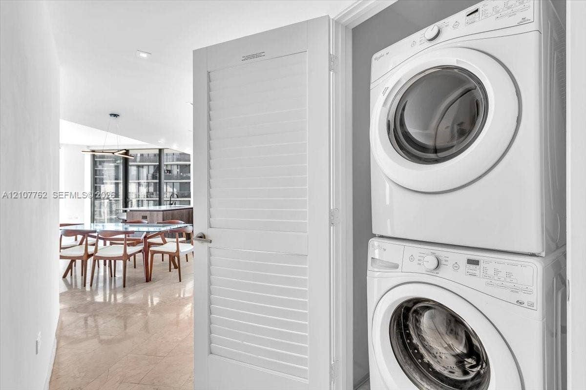 Stacked laundry unit featuring white front-load washer and dryer housed behind a white louvered door
