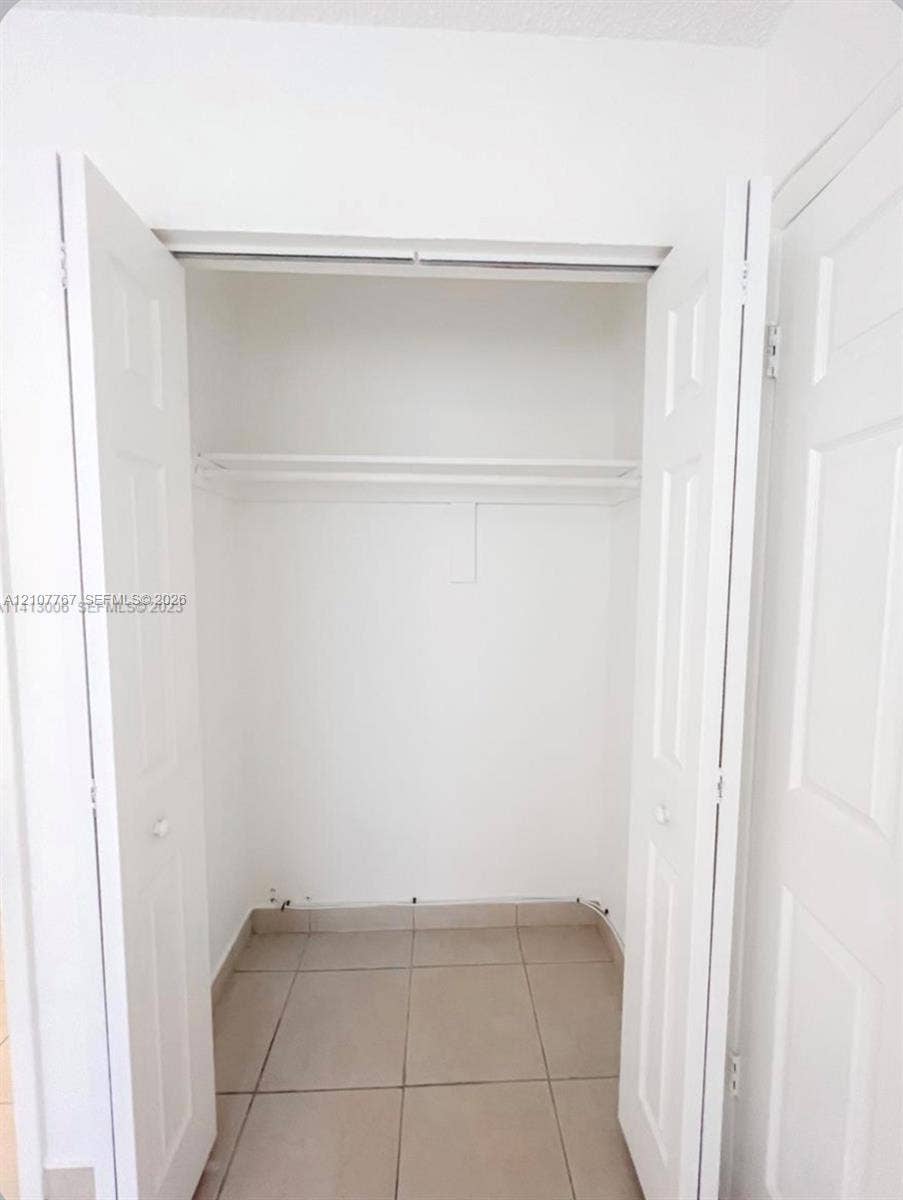 Reach-in closet featuring white paneled double doors, neutral tile flooring, and an integrated wire shelving unit