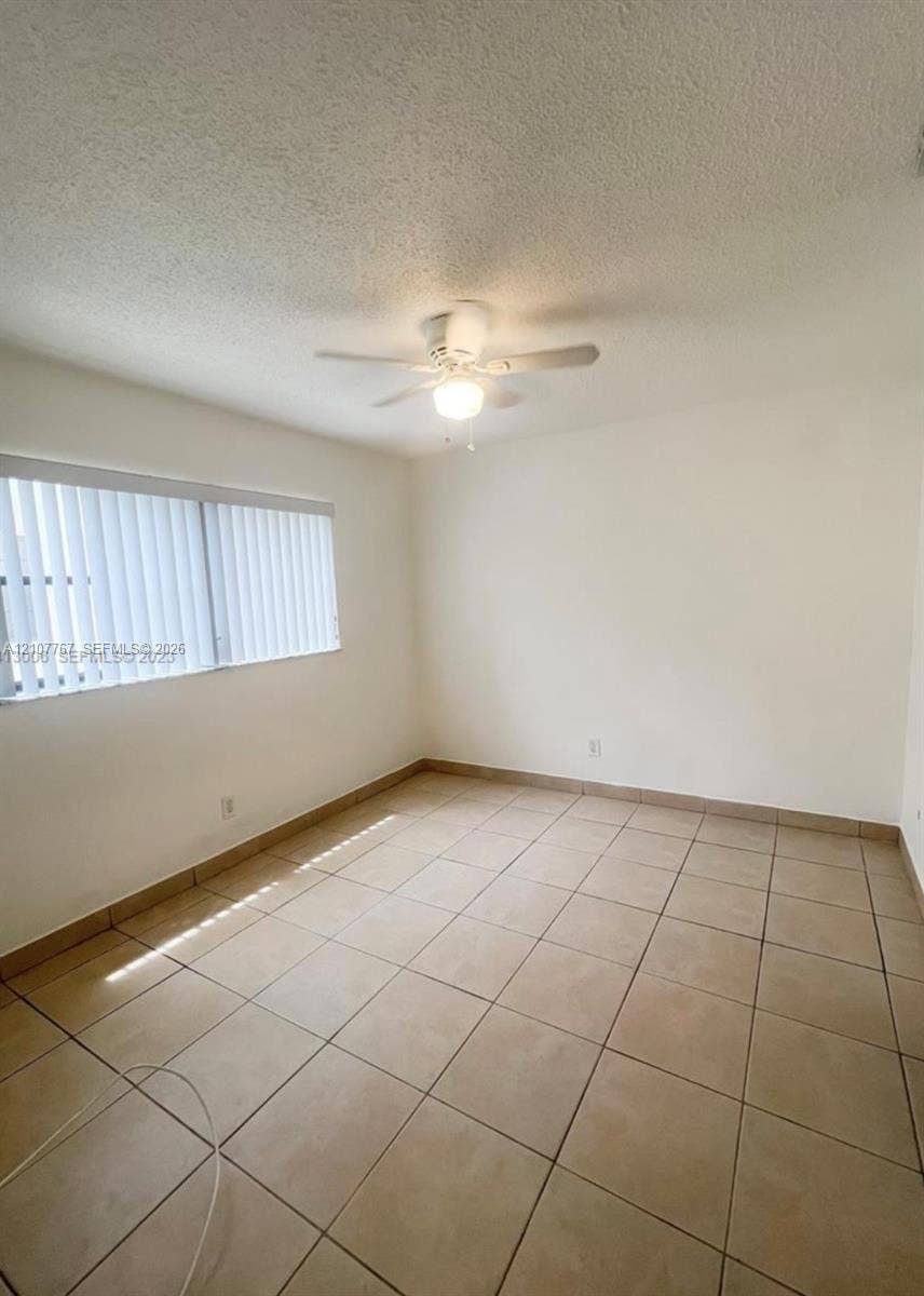 Neutral-toned tile flooring, white wall finishes, ceiling fan with integrated light fixture, and vertical window blinds