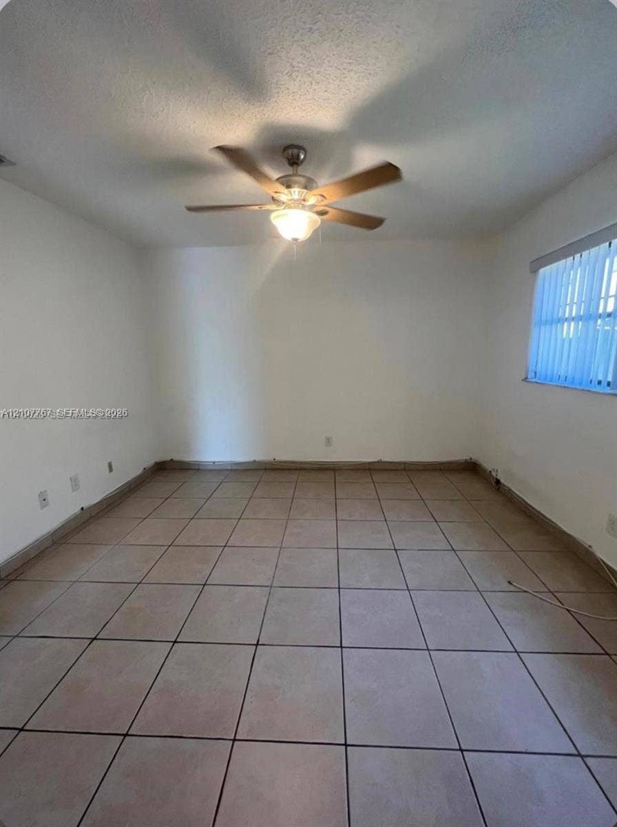 Room featuring neutral tile flooring, a central ceiling fan with integrated lighting, and horizontal window blinds