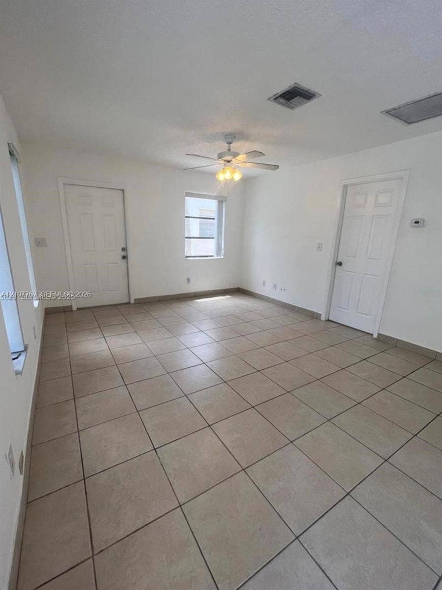 Interior space featuring large-format ceramic tile flooring, neutral walls, a multi-blade ceiling fan with integrated lighting, and solid-core interior doors