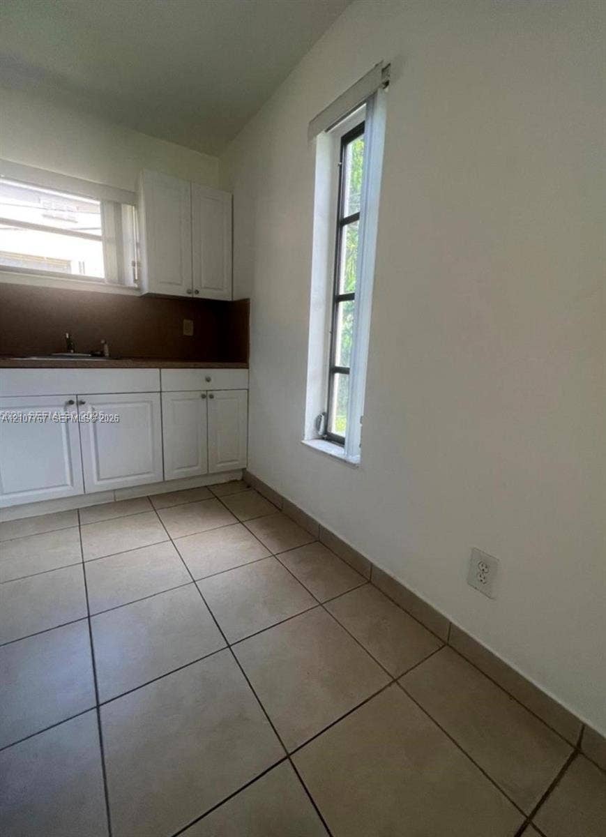 Kitchen featuring white shaker-style cabinetry, solid-surface countertops, neutral tile flooring, and vertical window placement