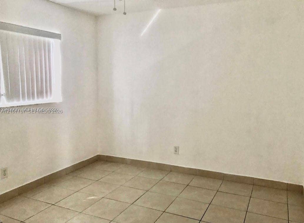 Neutral-toned interior space featuring large-format ceramic tile flooring, smooth wall finishes, and a window with vertical blinds