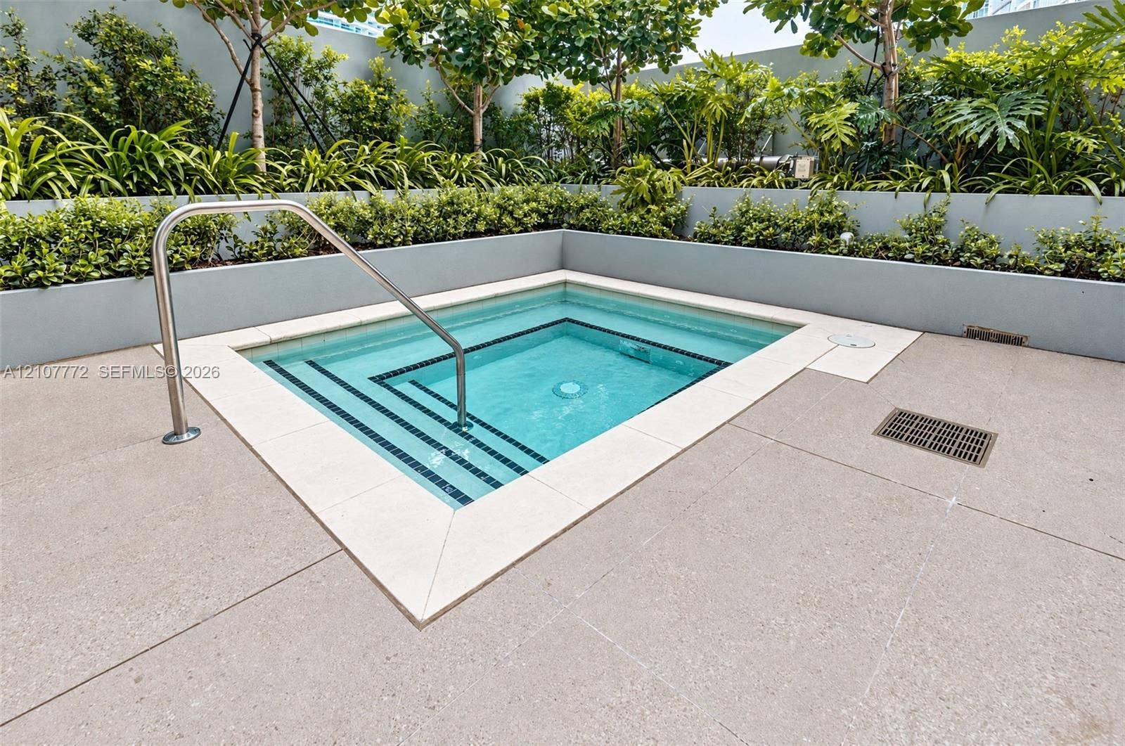 77 SE 5th Street, #1210, Miami, Miami, FL 33131 In-ground pool with integrated stepped entry and stainless steel handrail, bordered by stone-finish coping and tiered landscape planters with mature shrubbery
