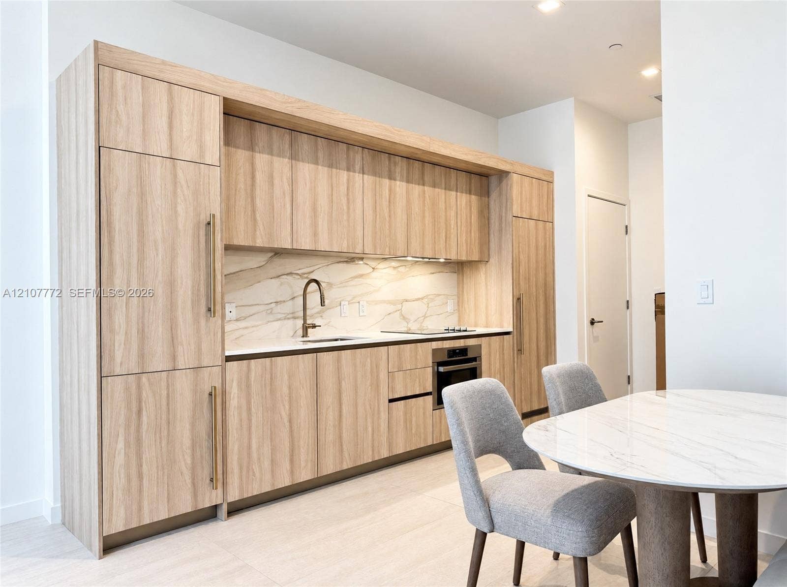 77 SE 5th Street, #1210, Miami, Miami, FL 33131 Modern kitchen featuring wood-finish cabinetry with integrated appliances, light-toned stone-style backsplash, undermount sink with a metallic pull-down faucet, and built-in cooktop and oven