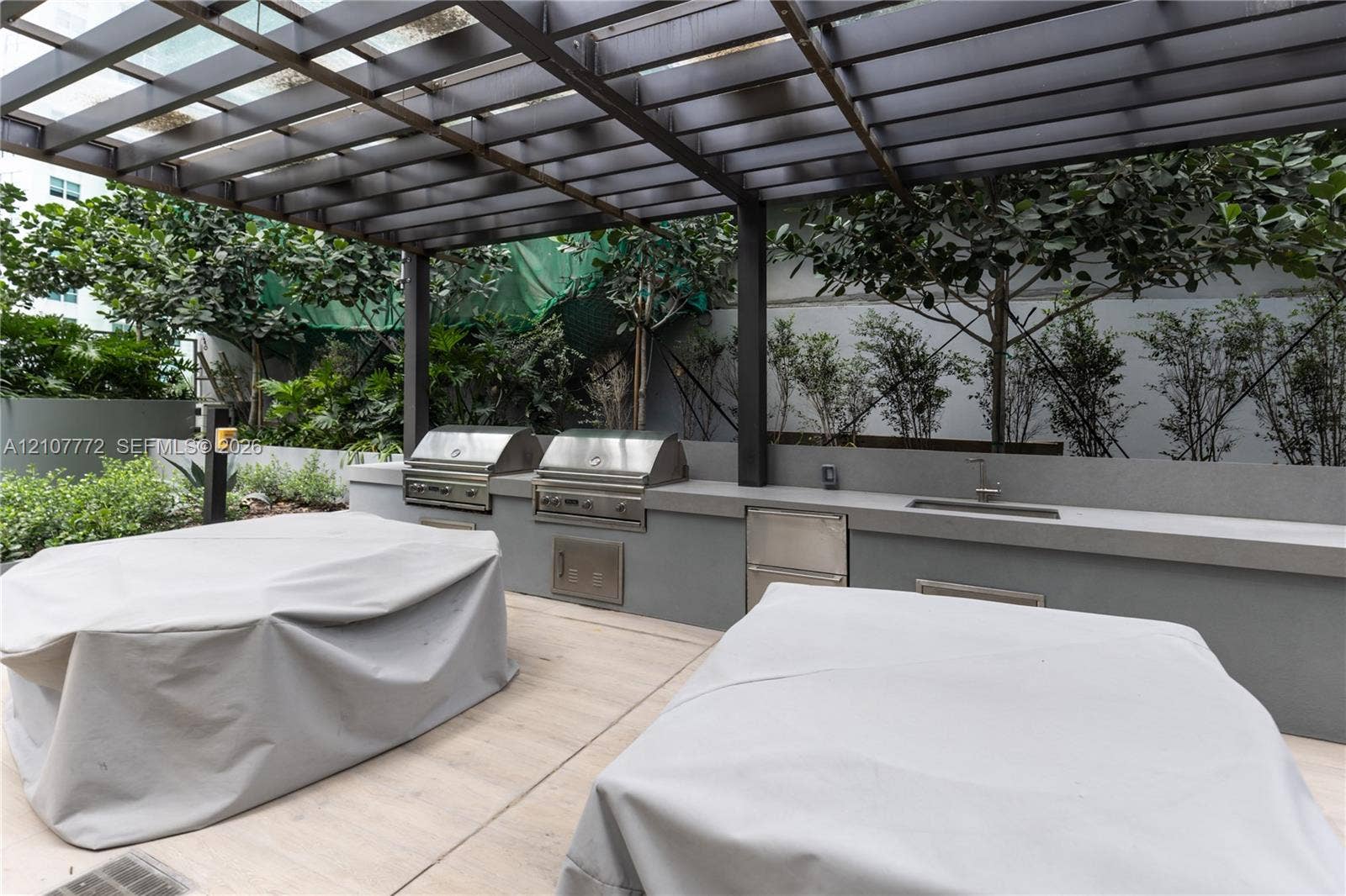 77 SE 5th Street, #1210, Miami, Miami, FL 33131 Outdoor kitchen featuring dual stainless steel grills, integrated stainless steel storage, a built-in sink, and a permanent pergola structure set over concrete hardscaping