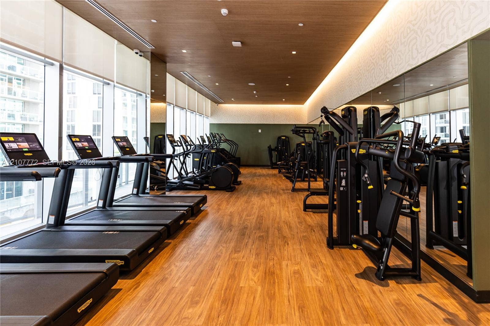 77 SE 5th Street, #1210, Miami, Miami, FL 33131 Fitness center featuring wood-finish flooring, floor-to-ceiling windows with roller shades, recessed cove lighting, and a full-length wall mirror