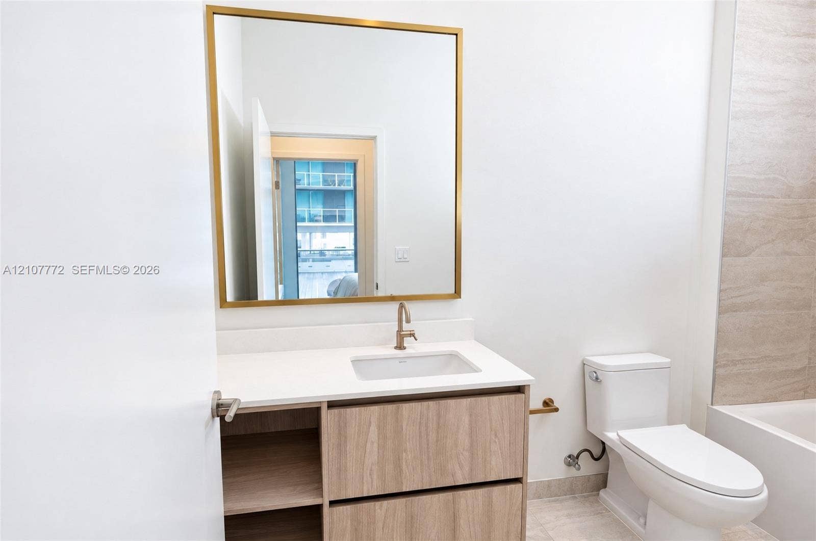 77 SE 5th Street, #1210, Miami, Miami, FL 33131 Bathroom featuring a vanity with wood-finish cabinetry, white countertop with an integrated basin, gold-toned hardware, and a square wall mirror with a metallic frame